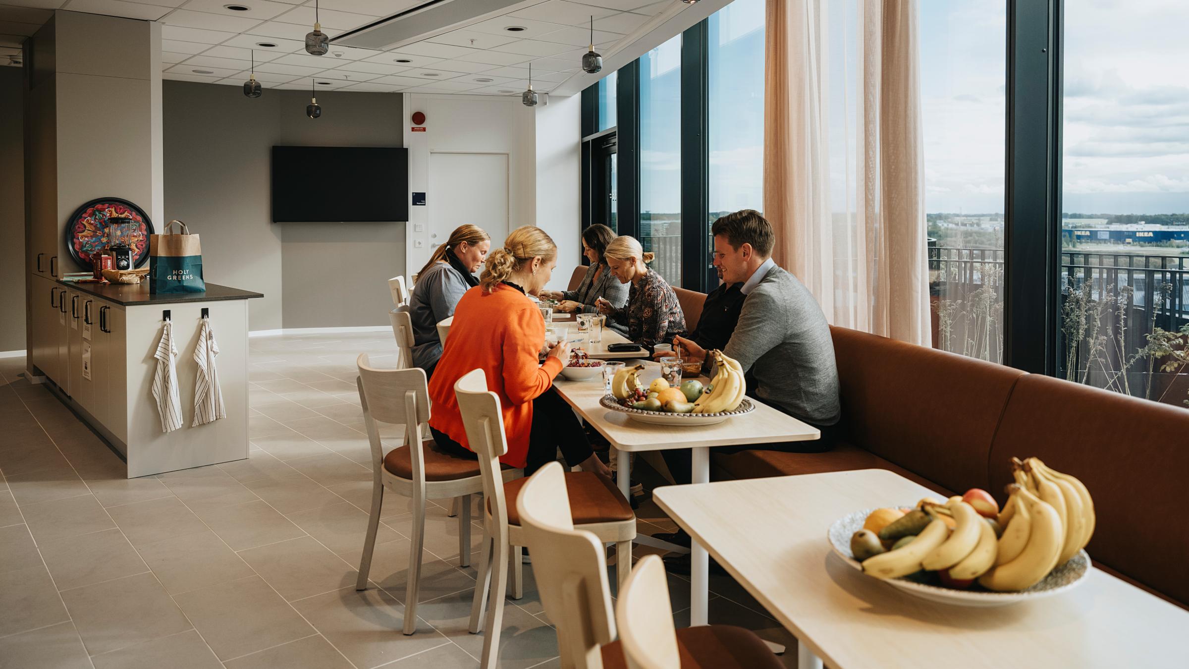 En stor del av inredningen består av möbler från företagets tidigare kontor, en medveten tanke för hållbarhet. Matsal med medarbetare som äter lunch.